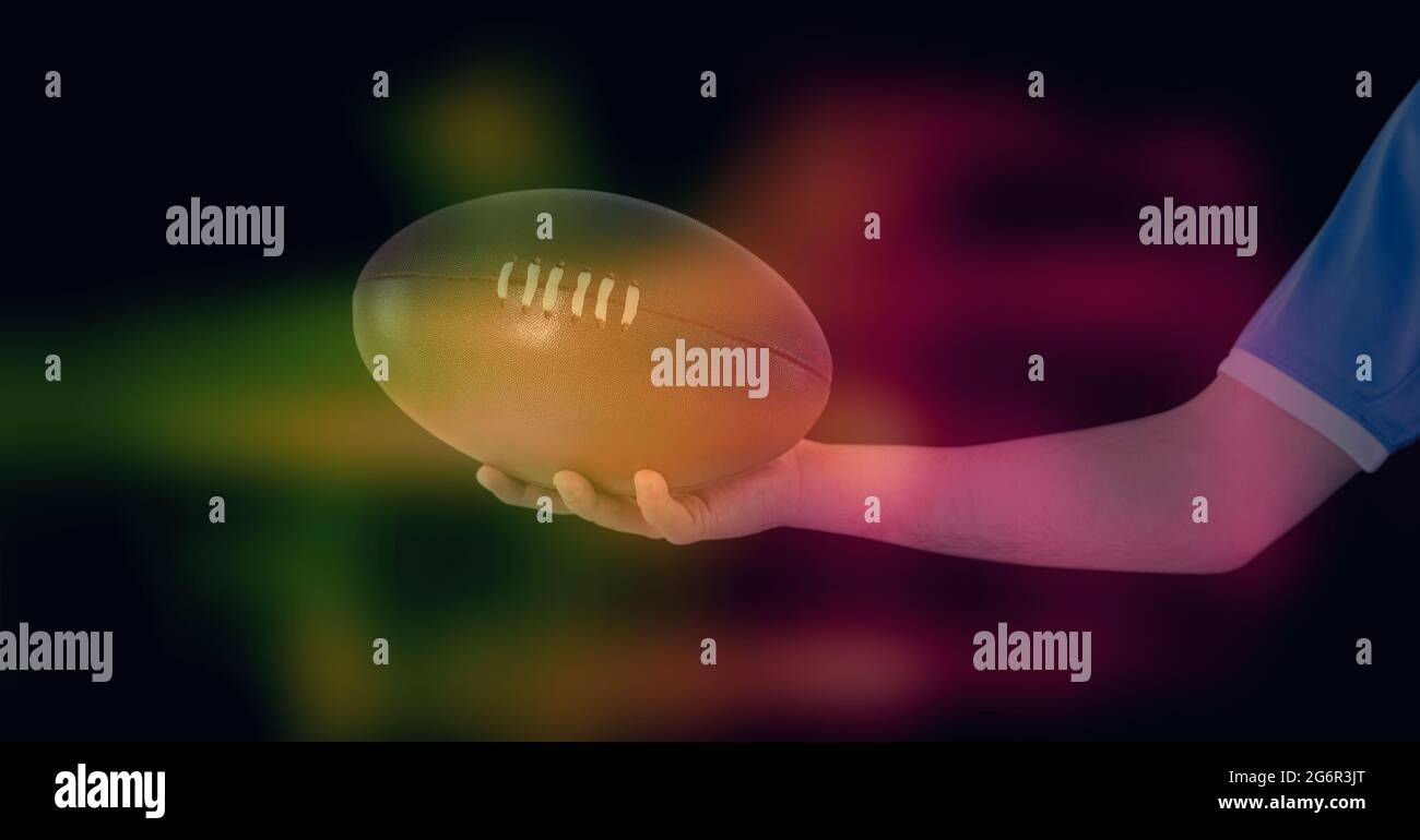 Composition of glowing yellow and red blur over arm of rugby player holding rugby ball, on black Stock Photo