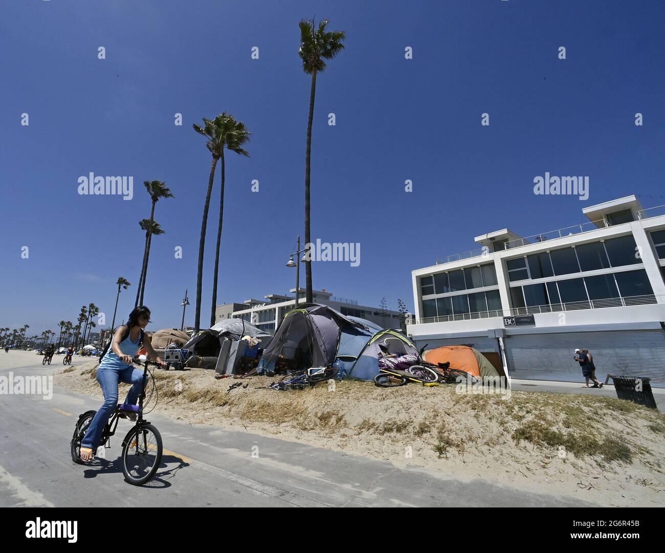 Los Angeles, United States. 08th July, 2021. A cyclist passes homeless encampments along the bike path in the Venice Beach area of Los Angeles on Wednesday, July 7, 2021. Fliers posted by the city outlined a five-week 'phased resumption of normal operations' with a 'comprehensive beachfront cleaning' of the area, which is under the jurisdiction of the city Recreation and Parks Department. The warning said the 'unhoused residents currently living in the park will be offered housing.' Photo by Jim Ruymen/UPI Credit: UPI/Alamy Live News Stock Photo