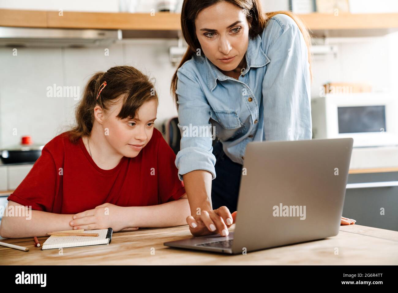 White woman helping her daughter with down syndrome using laptop at home Stock Photo