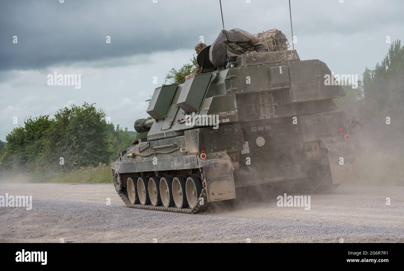 british army military AS-90 (Gun Equipment 155mm L131) armoured self-propelled howitzer gun hurtling along a stone track creating clouds of dust in a Stock Photo