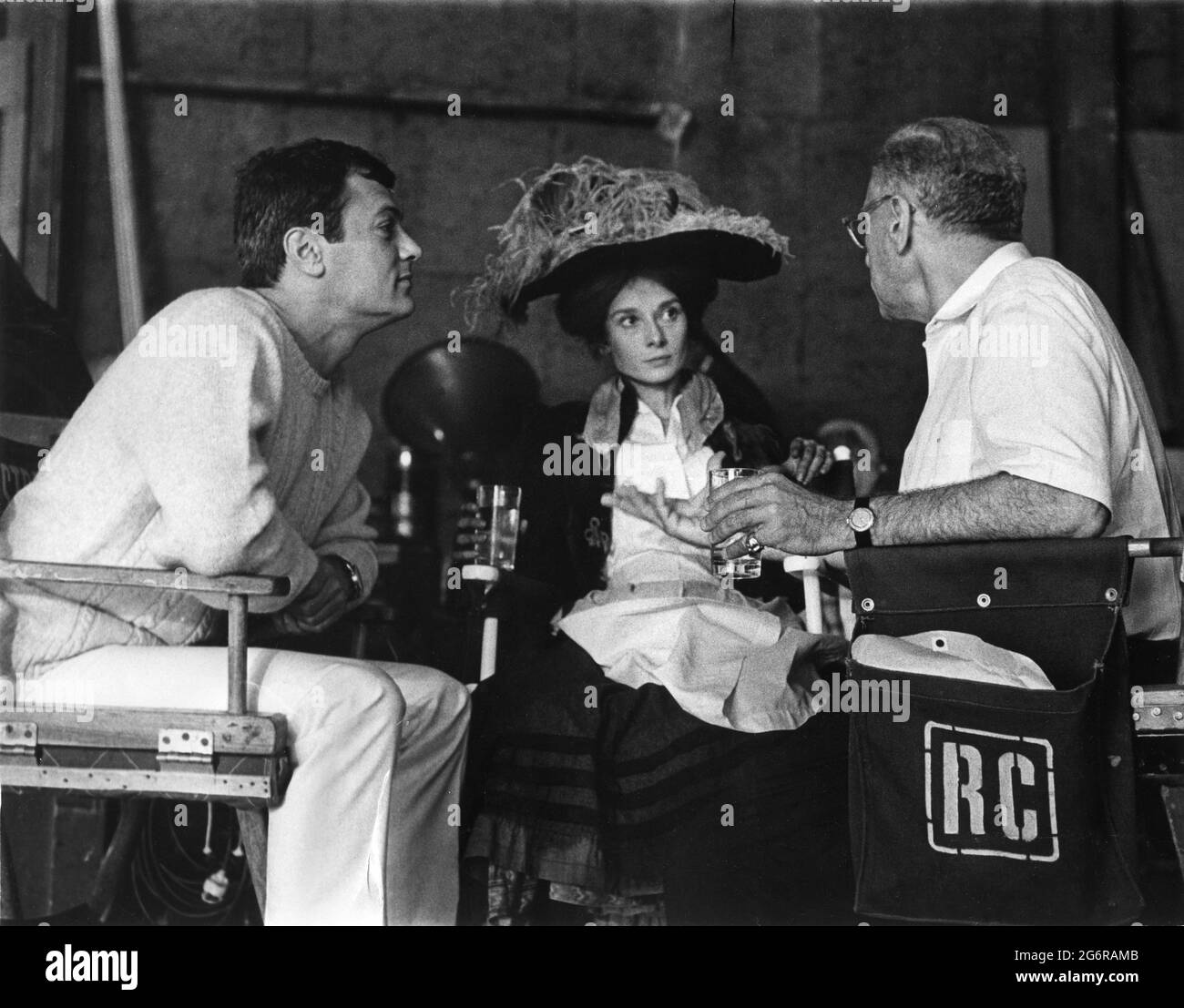 Set Visitor TONY CURTIS with AUDREY HEPBURN and Director GEORGE CUKOR on set candid during filming of MY FAIR LADY 1964 director GEORGE CUKOR from the Broadway musical adapted from the play Pygmalion by George Bernard Shaw screenplay book and lyrics Alan Jay Lerner  music Frederick Loewe production design and costumes Cecil Beaton producer Jack L.Warner Warner Bros. Stock Photo