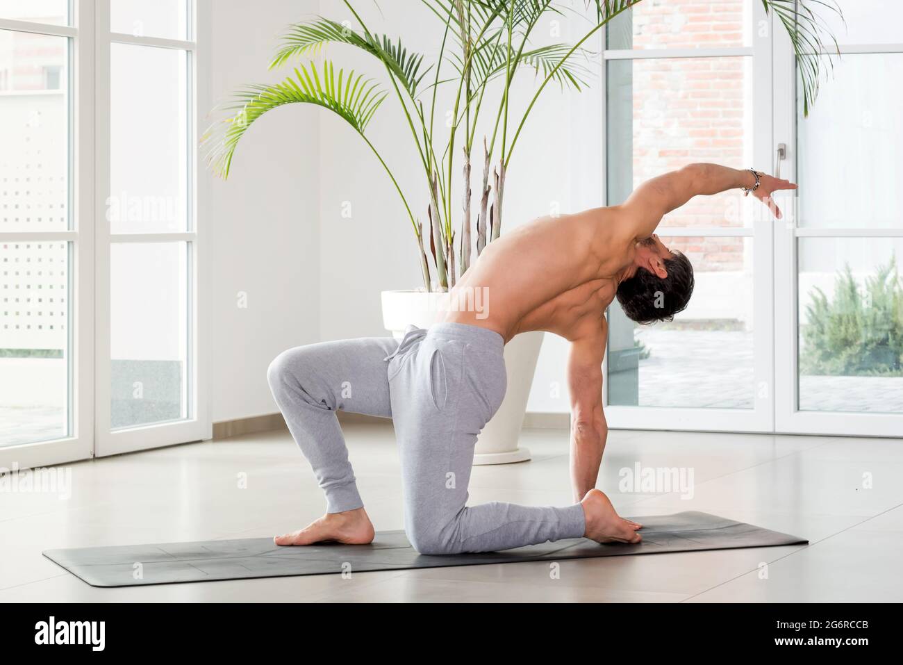 Man doing a backbend and twist yoga pose to increase mobility and flexibility of his body and muscles in a high key gym with copyspace in a health and Stock Photo