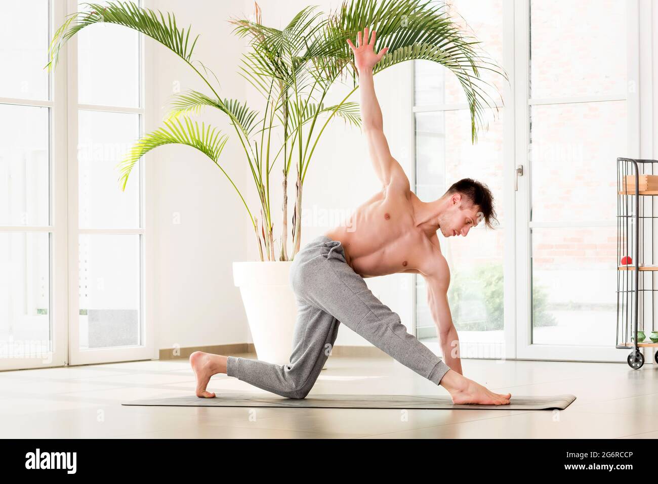 Young man doing a Parivrtta trikonosana or revolved triangle yoga pose in a high key gym with copyspace in a healthy active lifestyle concept Stock Photo