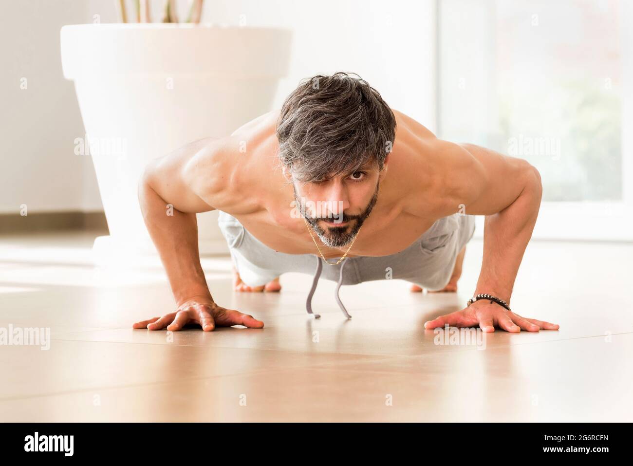 Determined athletic man exercising a plank variation or a push-up exercise during indoors fitness routine for muscular strength and body control at ho Stock Photo