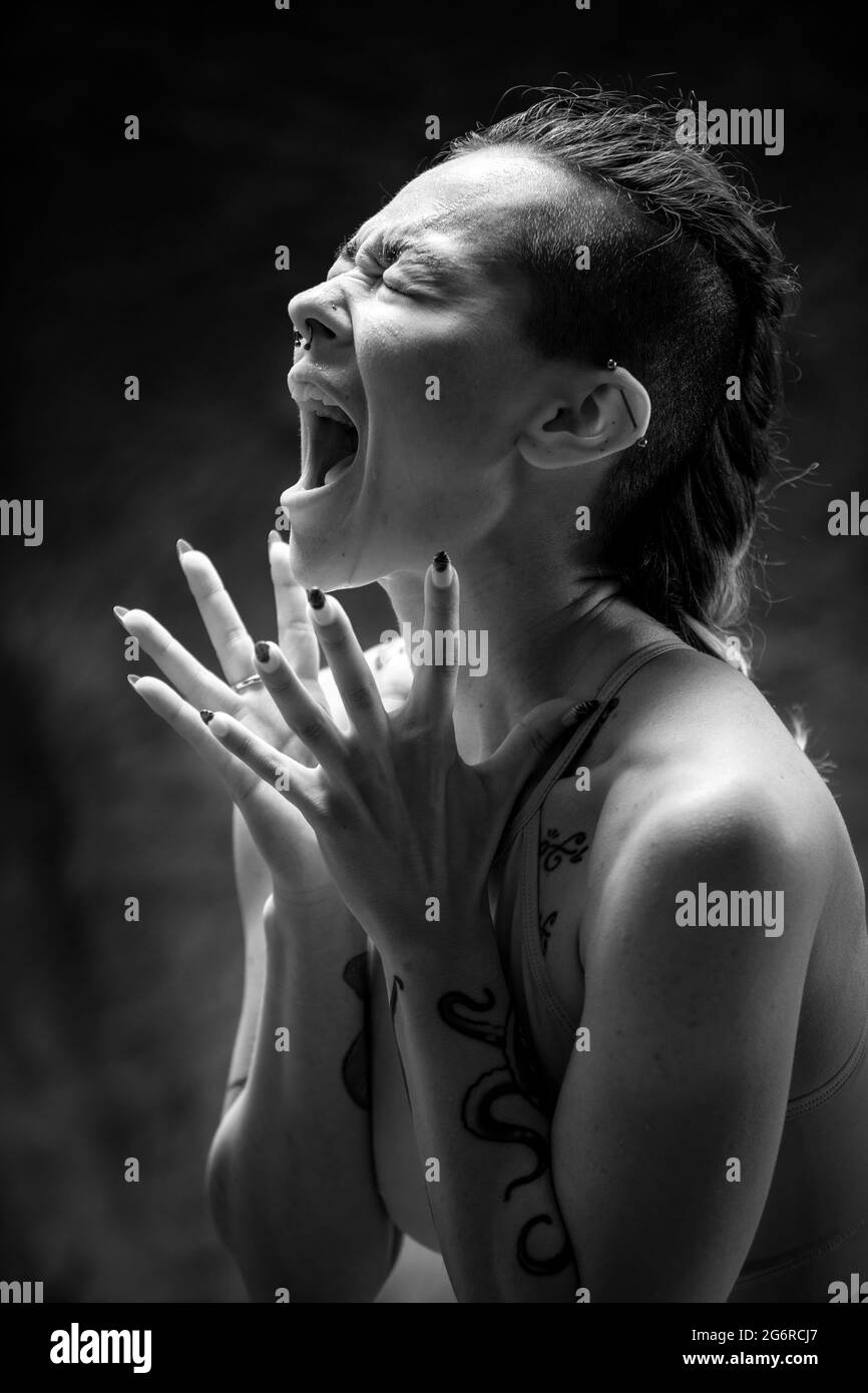 A young woman wearing gymwear, standing in front of a backdrop. She is screaming out loud and her hands are outstretched. Stock Photo