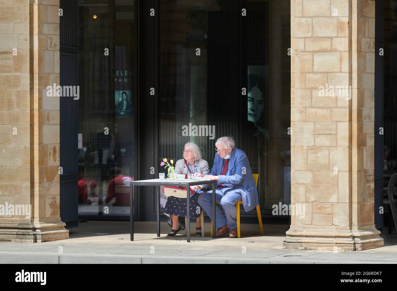 A senior couple have lunch outside the café at Weston library, university of Oxford, England, on a sunny summer day. Stock Photo