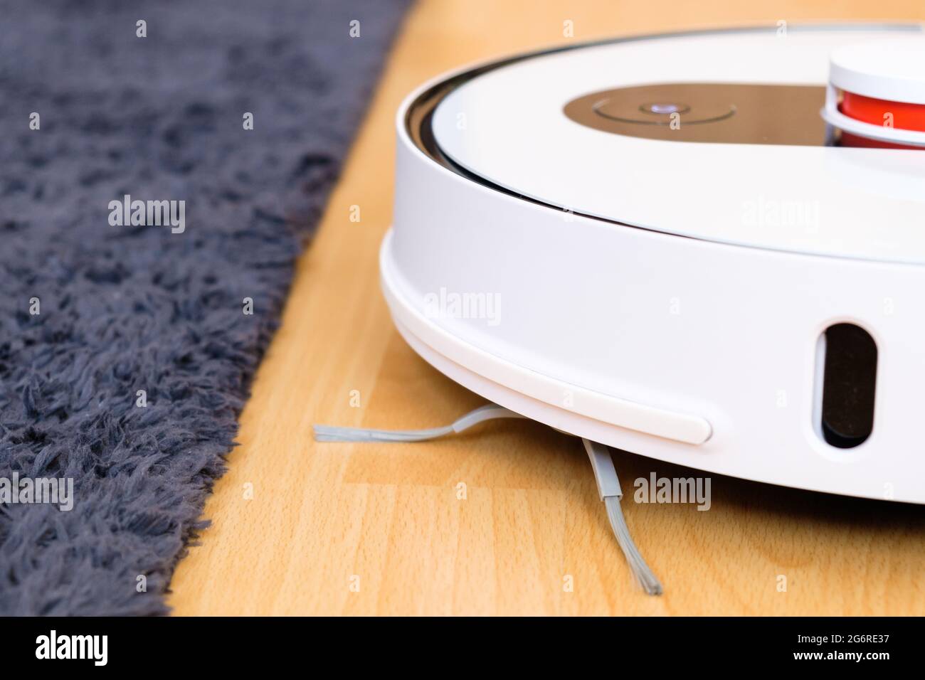 Robot vacuum cleaner performs cleaning of the wooden floor near the carpet. Housekeeping smart technology Stock Photo