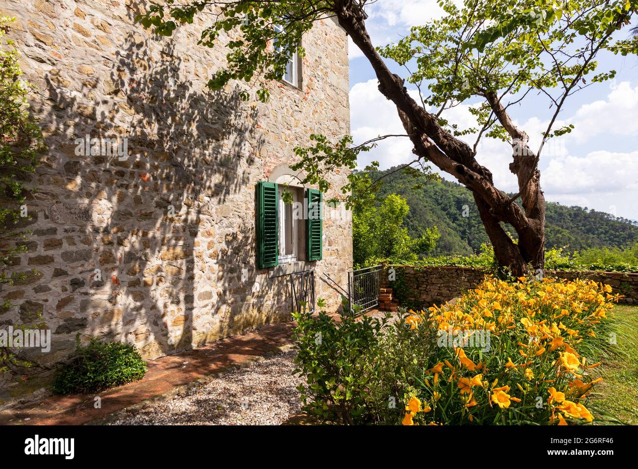 Detail of a wall of an ancient stone house with a flower garden aside ...
