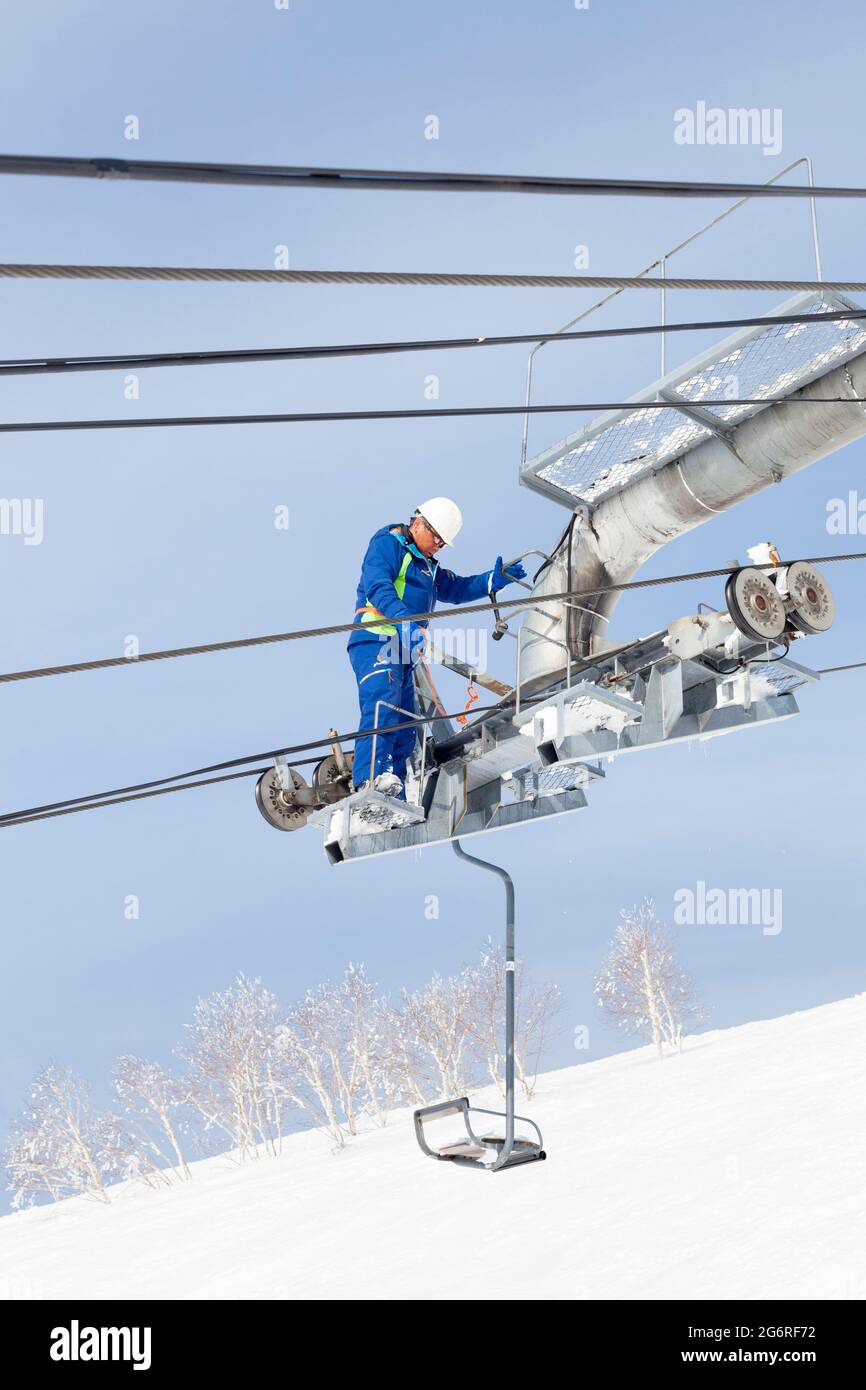 NISEKO, JAPAN - March 9 : A maintenance engineer inspects a chair lift at Niseko, Japan on 9th March 2012.The ski slopes and snow covered trees of Nis Stock Photo