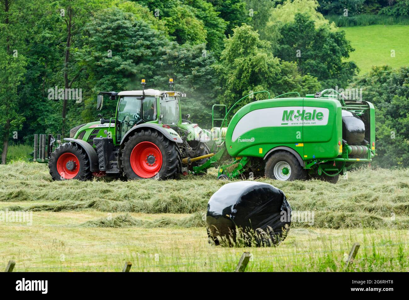 Hay & silage making (farmer in farm tractor at work in scenic rural field, collecting dry grass, wrapped round bale in baler) - Yorkshire England, UK. Stock Photo