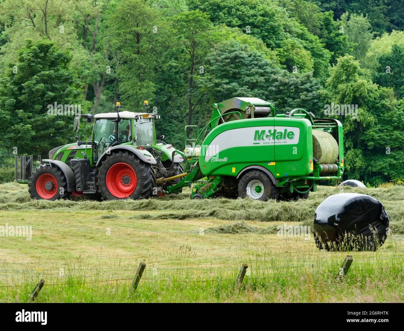 Hay & silage making (farmer in farm tractor at work in rural field, collecting cut dry grass, unwrapped round bale in baler) - Yorkshire England, UK. Stock Photo