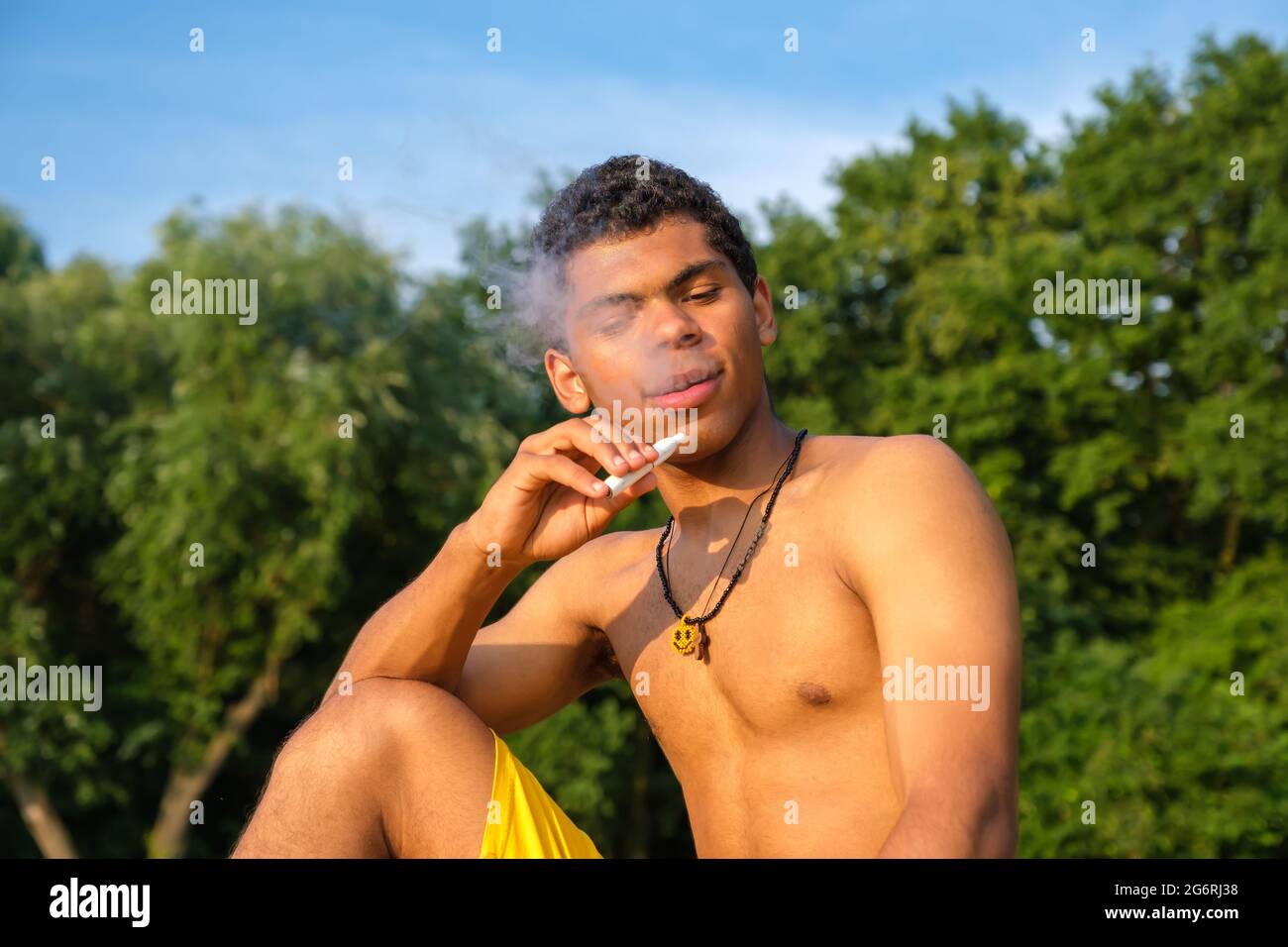 Brazilian young man vaping e-cigarette with e-liquid outdoors in summer Stock Photo