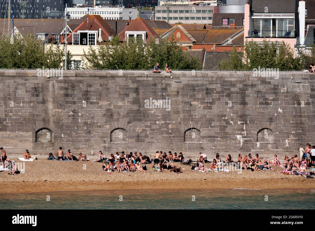 young people enjoy summer sunshine on a small shingle beach at Portsmouth harbour,Hampshire,England Stock Photo