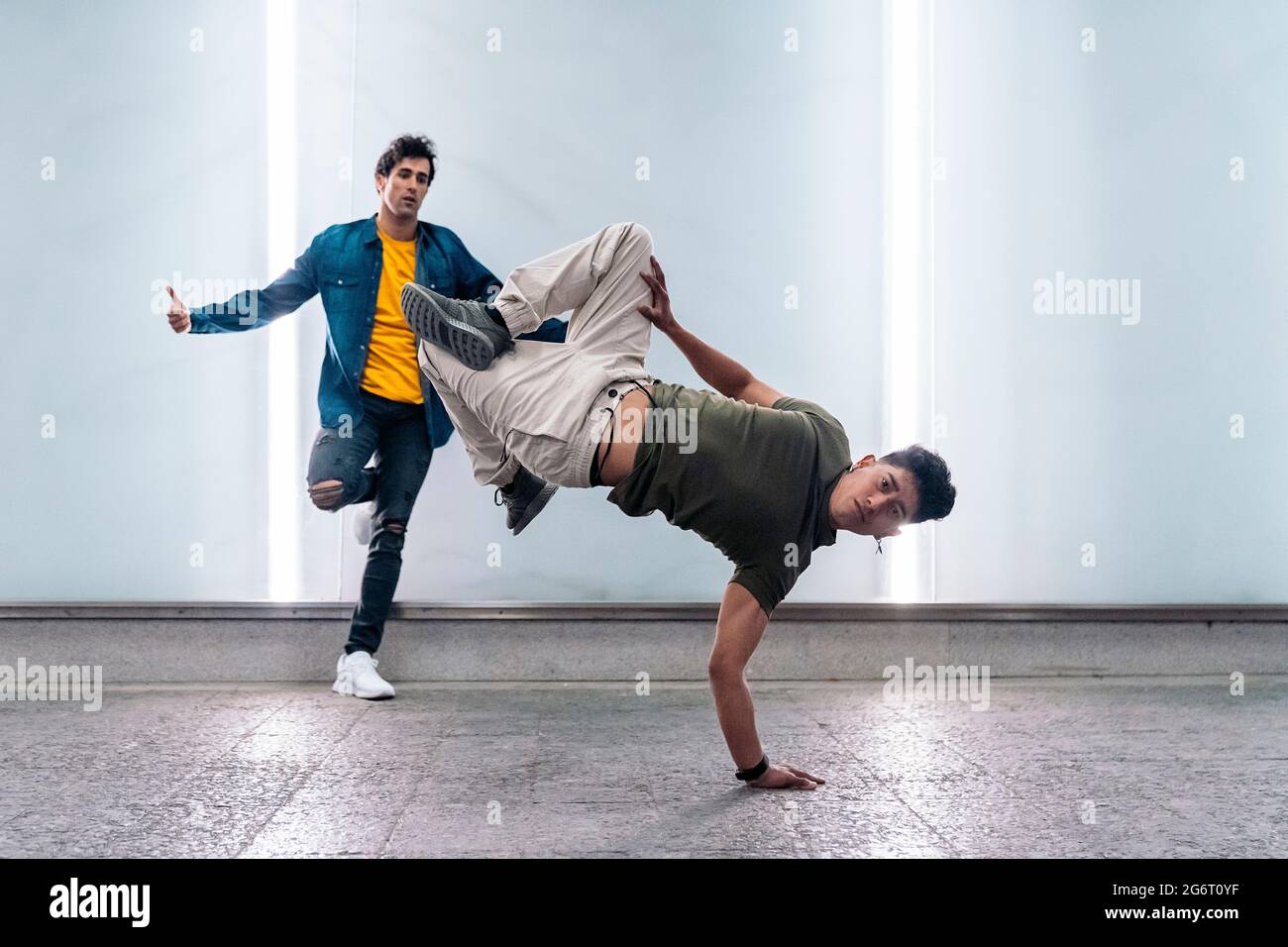 Two multi-ethnic friends dancing break dance and having fun against white wall with lights. Stock Photo