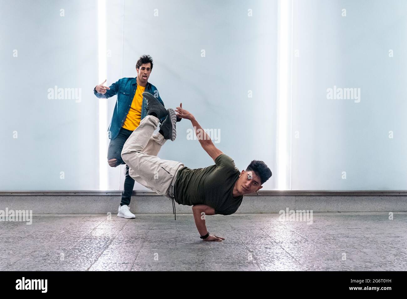 Amazing young men practicing break dance together against white wall with lights. Stock Photo