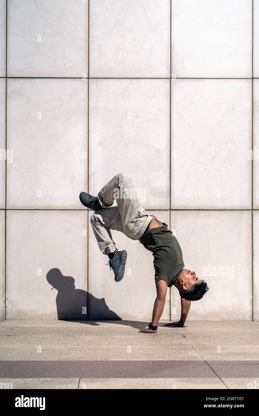 Confident young boy doing break dance dances against white wall in the street. Stock Photo