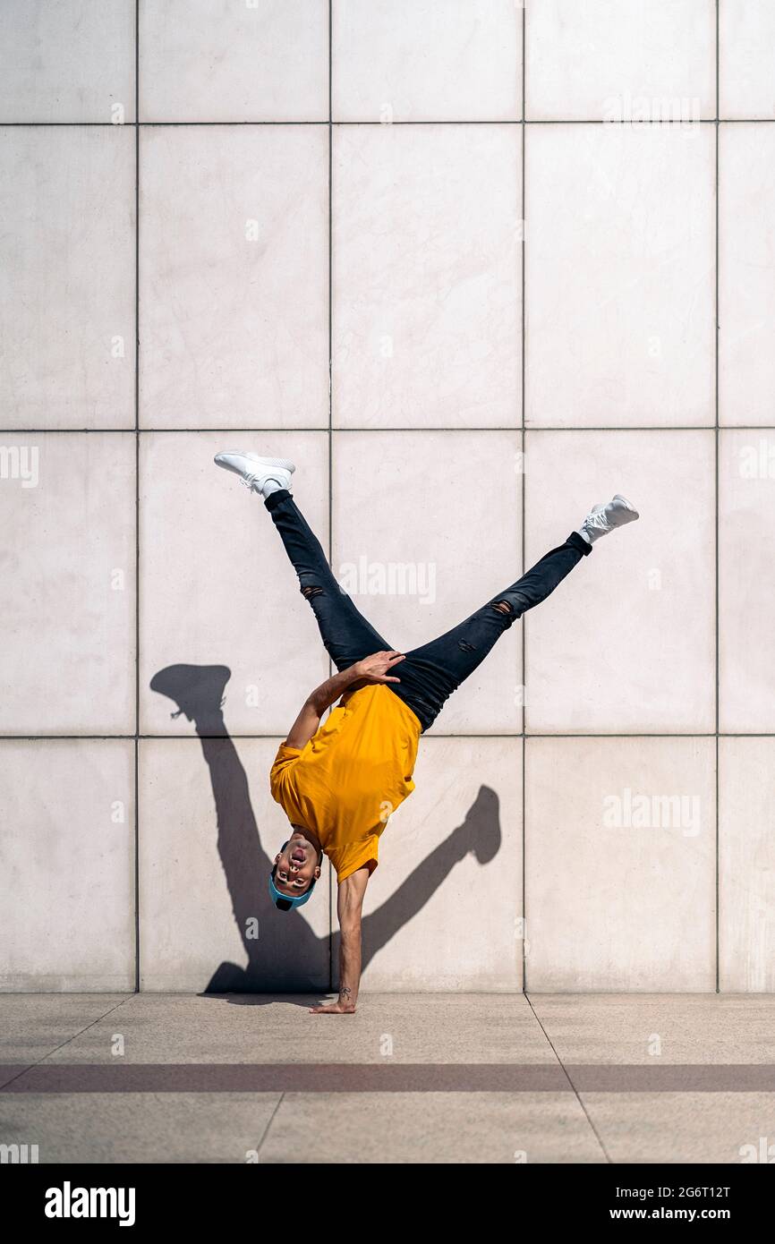 Confident young boy doing break dance dances against white wall in the street. Stock Photo