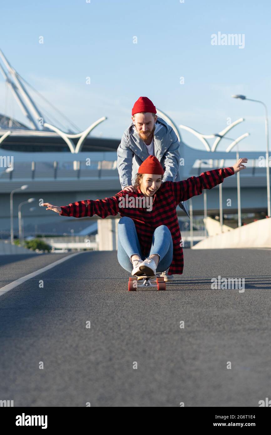 Young hipster couple have fun on longboard outdoors riding city road cheerful laughing together Stock Photo