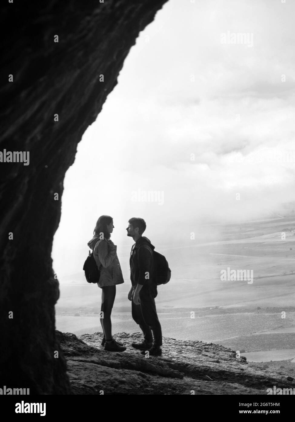 Couple inside a cave against cloudy sky. Scenic rear view of a man and a woman walking in outstanding caves against beautiful landscape in Cuevas de Stock Photo