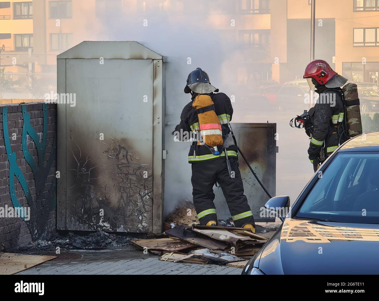 Firefighters extinguishing garbage can fire in car park Stock Photo
