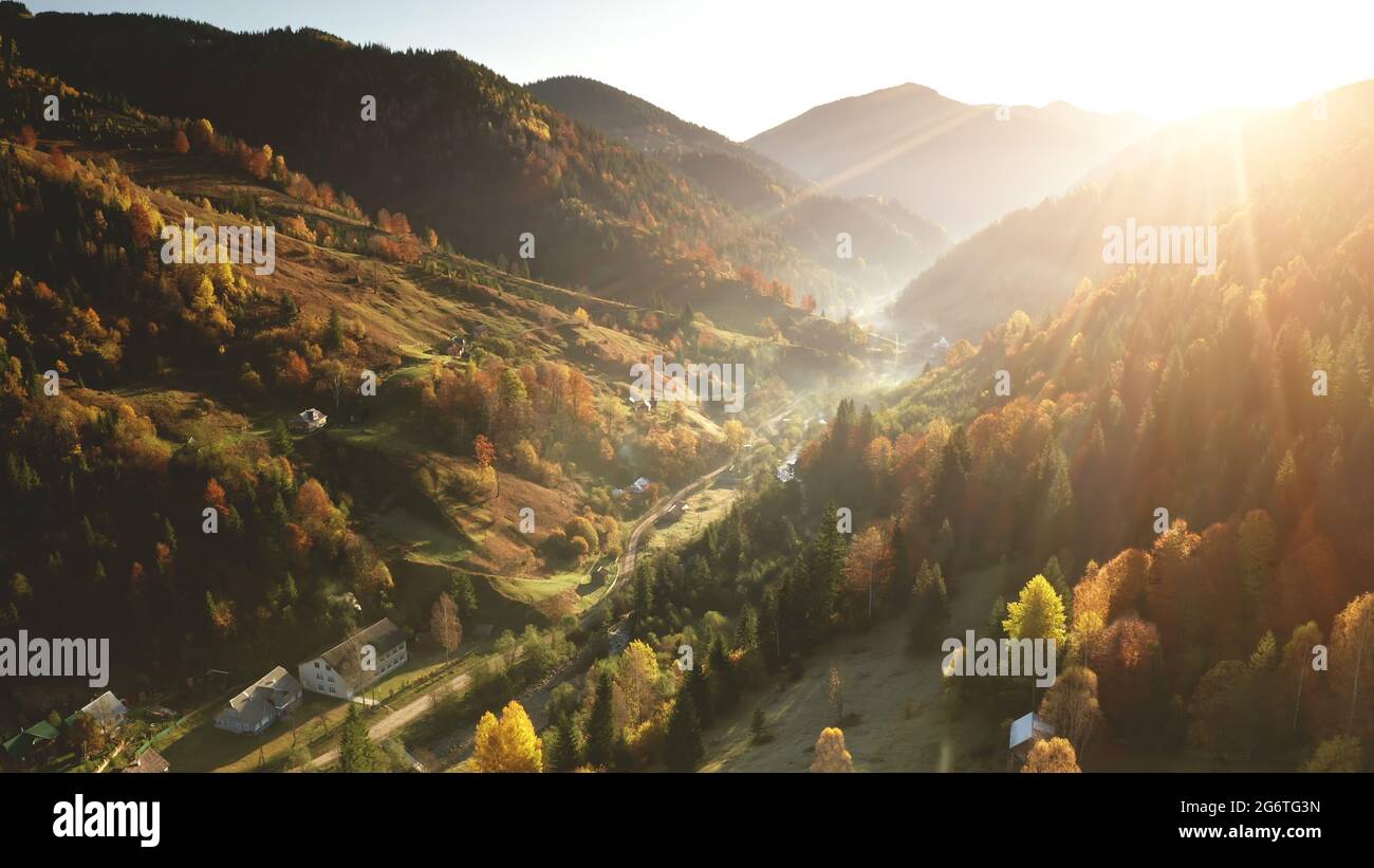 Aerial mist over mountain village at sun day. Autumn nobody nature landscape. Cottages on mount hills. Green pine trees forest at rural road in fog. Unknown misty Carpathian ridges, Ukraine, Europe Stock Photo