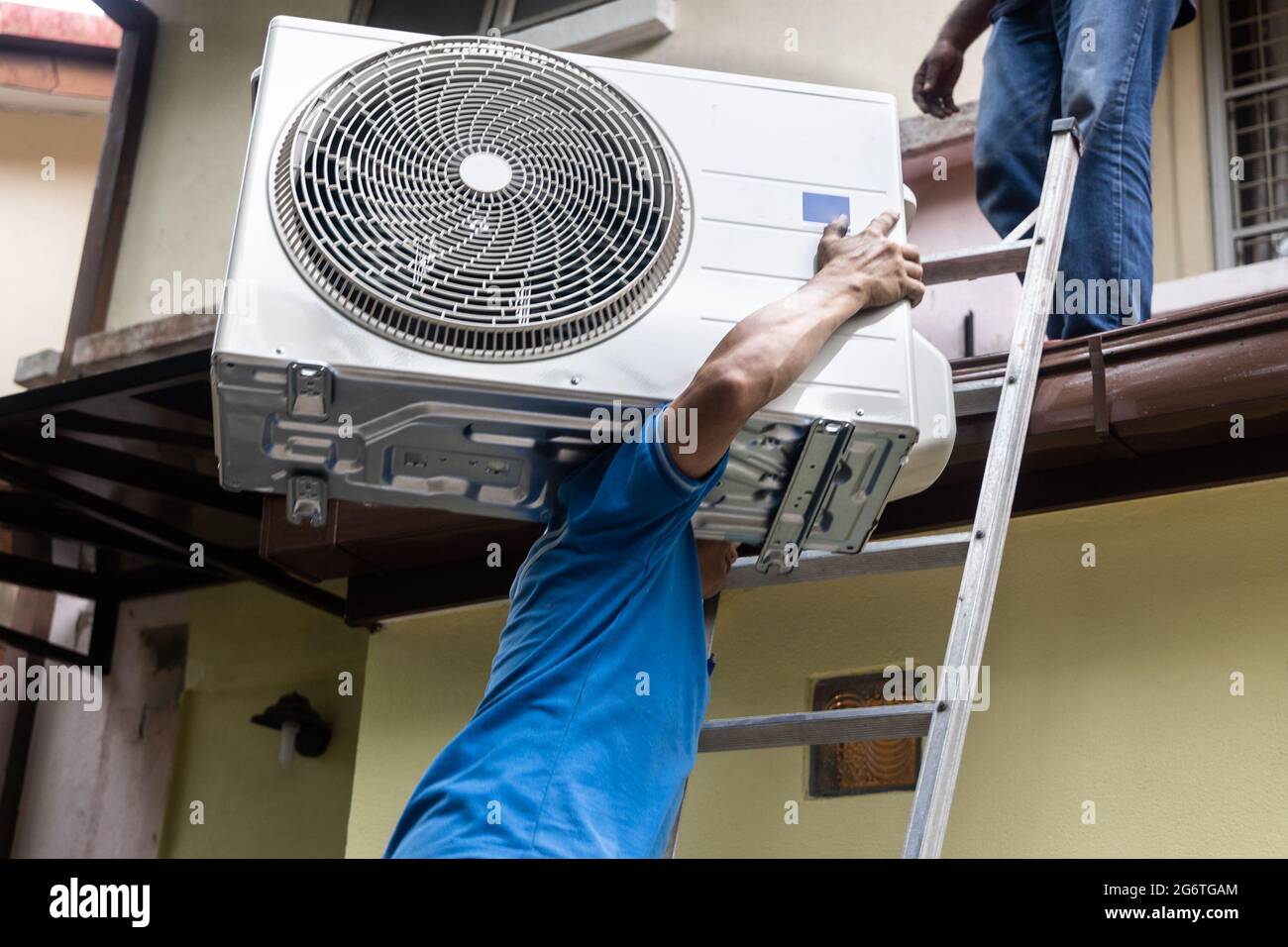 Technician transporting outdoor air conditioner compressor unit onto roof for installatiion