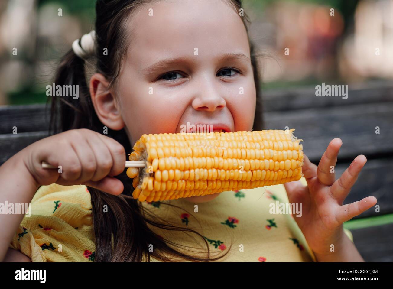 close-up portrait in detail of a girl biting sweet hot corn on a hiking trip in a summer green forest Stock Photo