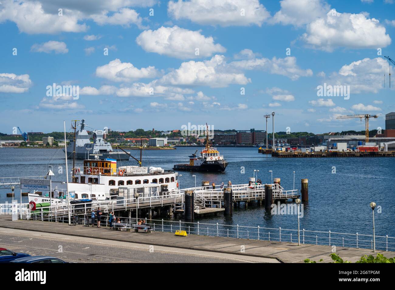 Kiel Werft und Seebrücke, auf dem Wasser ein Schlepper und ein gerade auslaufendes Kriegsschiff zu einer Probefahrt Stock Photo