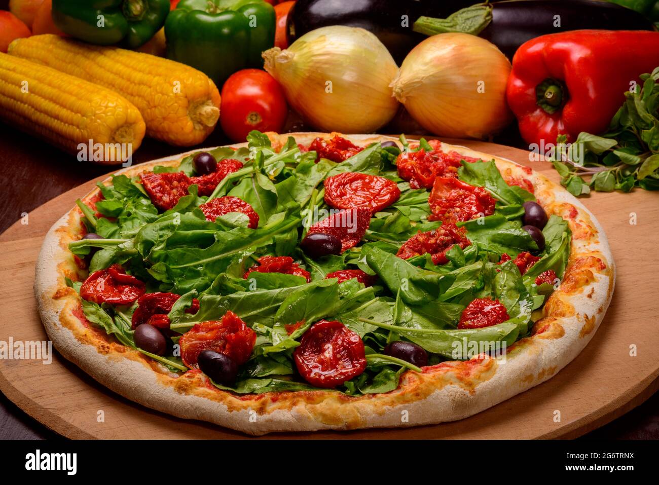 Arugula and sun dried tomato pizza on wooden board and vegetables in