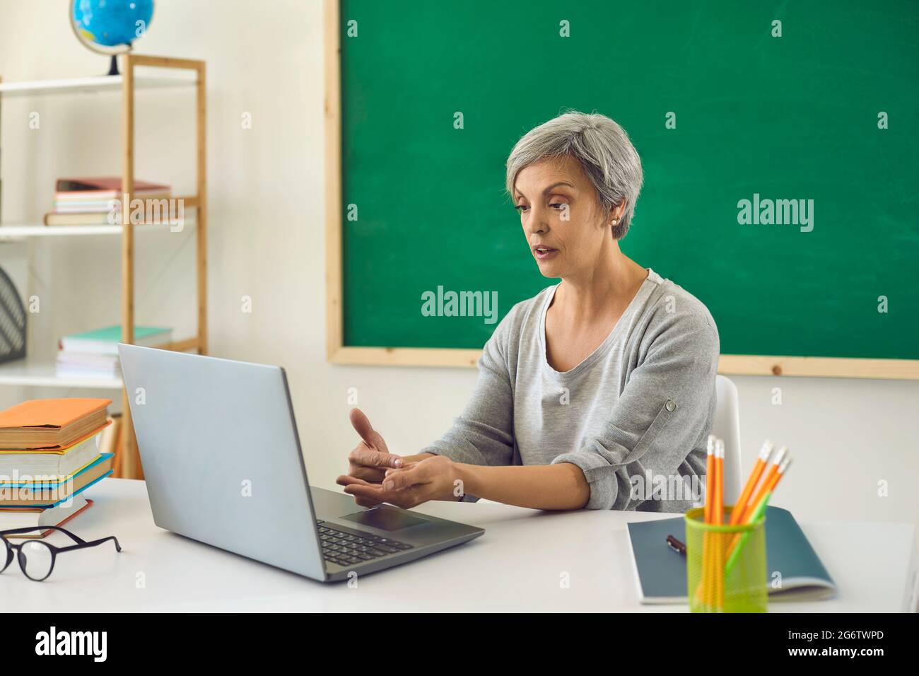 Online learning education. Female senior teacher is teaching students or schoolchildren using a video conference has a laptop in the classroom. Stock Photo