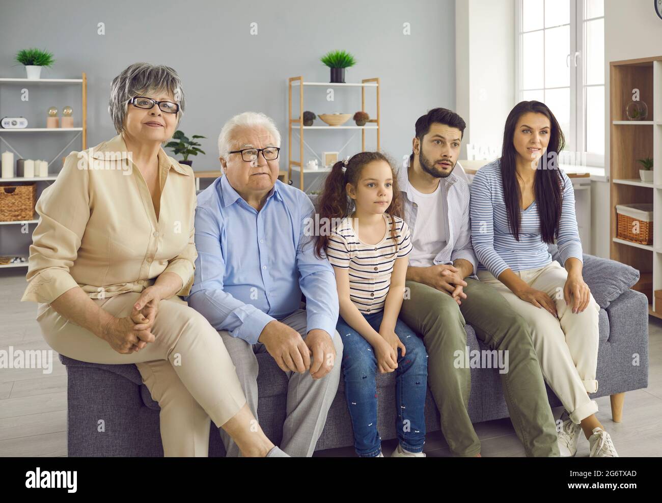 Multigenerational family sitting on couch at home and watching television all together Stock Photo