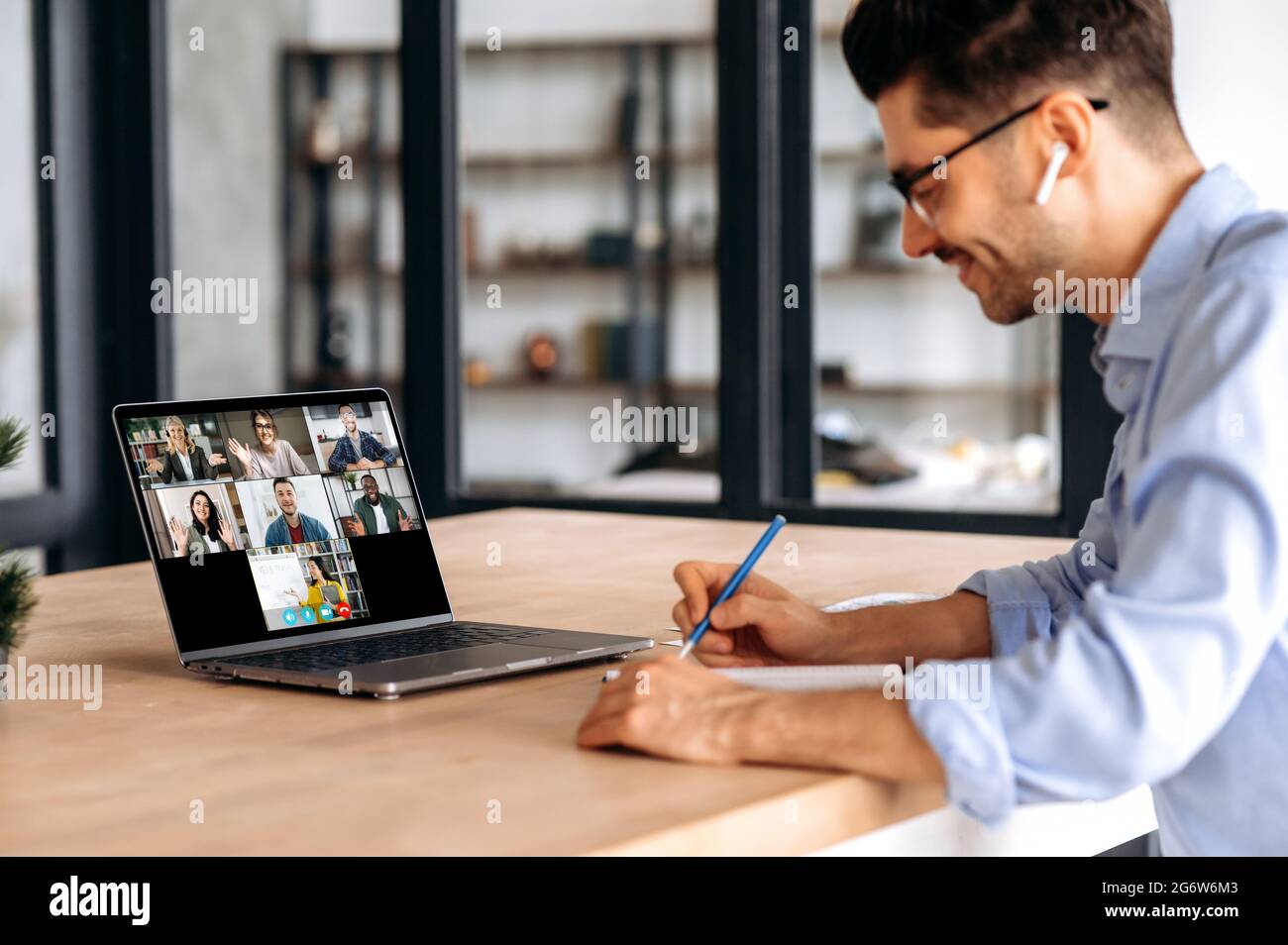 Video conference with teacher and students. Clever caucasian guy watching lesson online and studying distantly. Young man takes notes, listening lecture from female teacher on video call Stock Photo