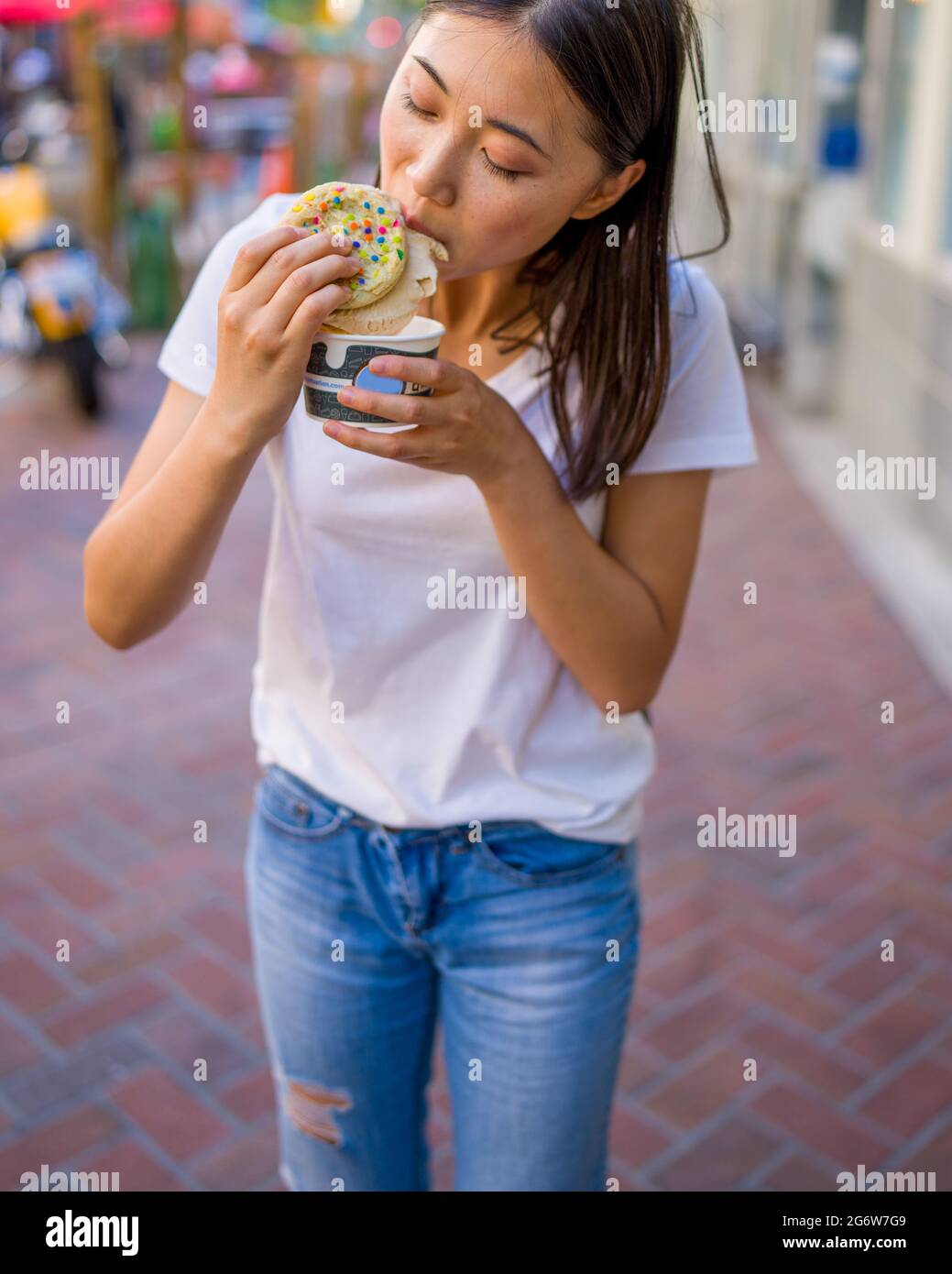 Happy Young Asian Woman Eating an Ice Cream Sandwich in an Urban Setting Stock Photo
