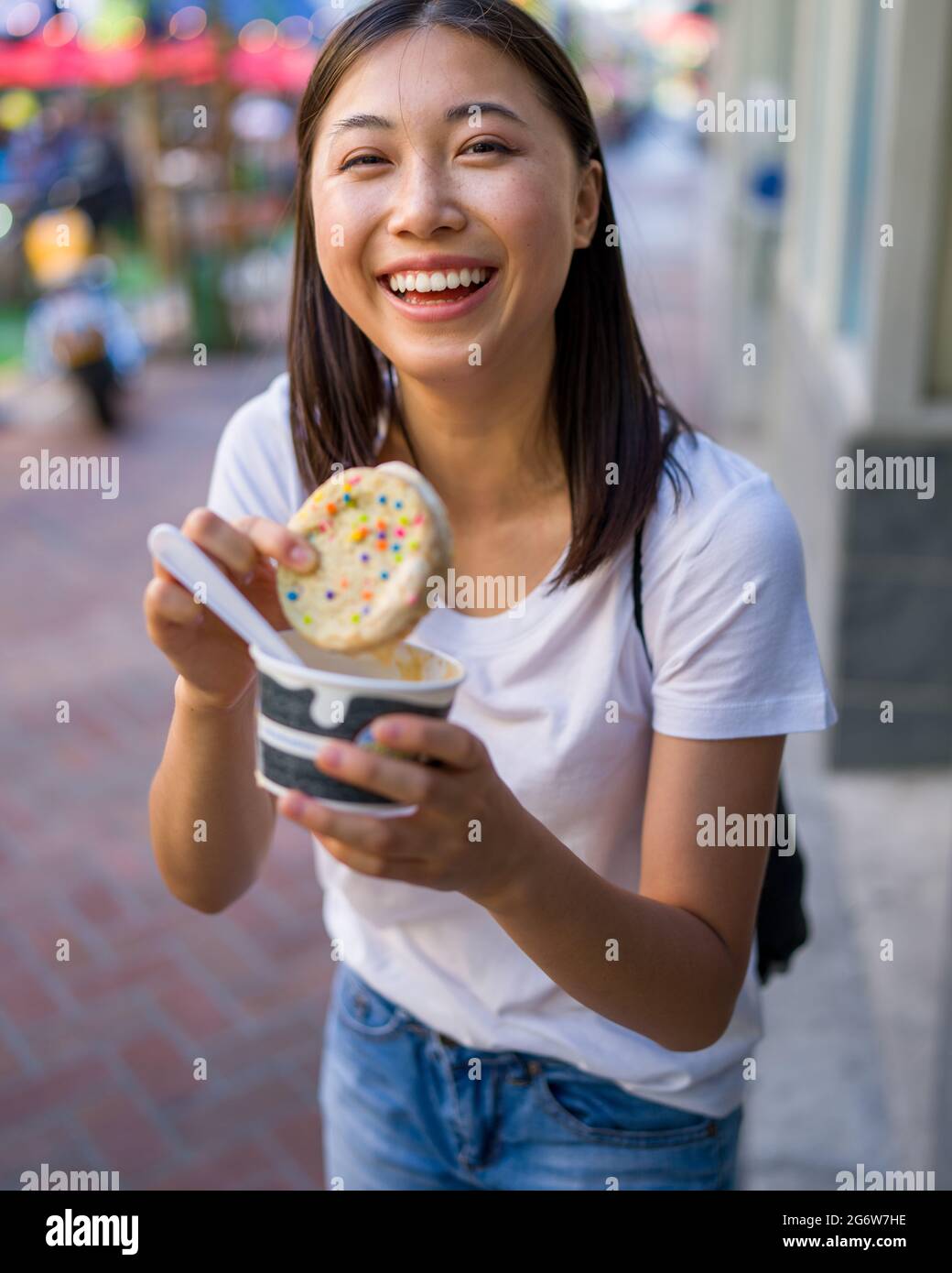 Happy Young Asian Woman Eating an Ice Cream Sandwich in an Urban Setting Stock Photo