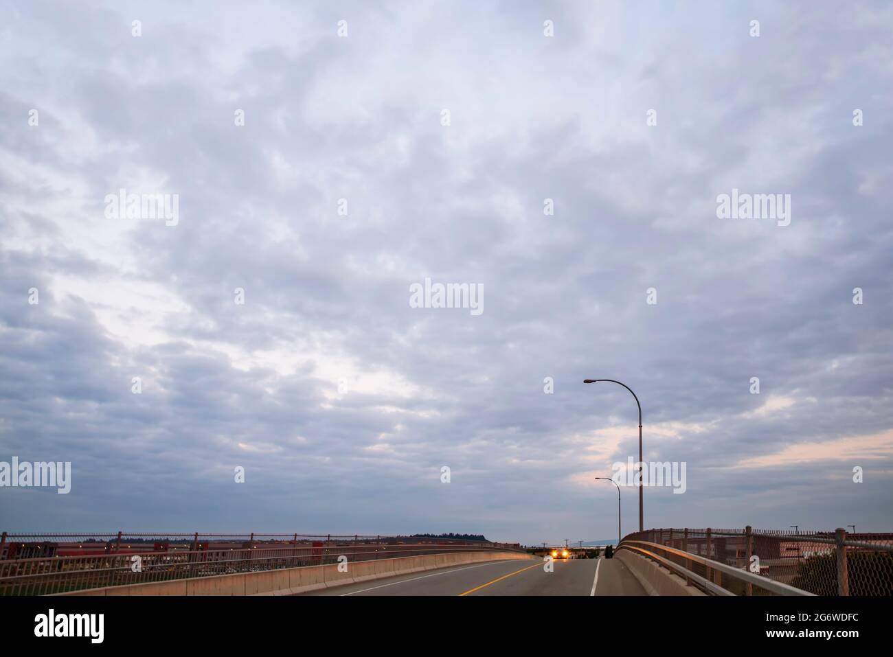 blue-pink evening clouds over the car viaduct, the glowing headlights of the car moving forward along the bridge. Stock Photo
