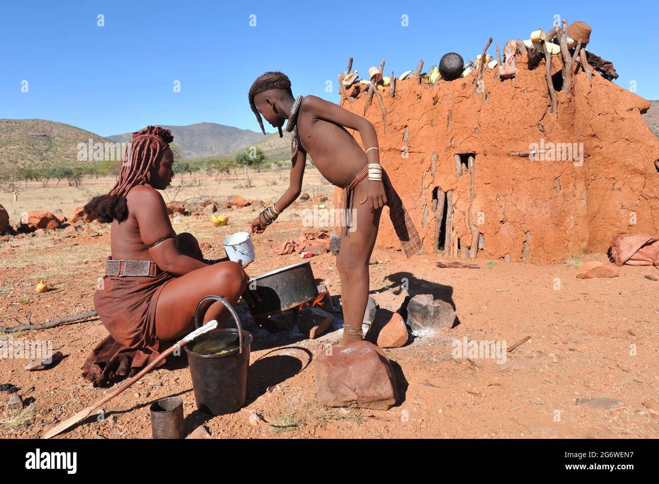 NAMIBIA. HIMBA WOMAN AND HER DAUGHTER MAKING SOME FOOD IN THEIR VILLAGE. THE HIMBA VILLAGE, OR KRAAL, IS COMPOSED OF FEW WOODEN AND CLAY HUTS WITH ONE Stock Photo
