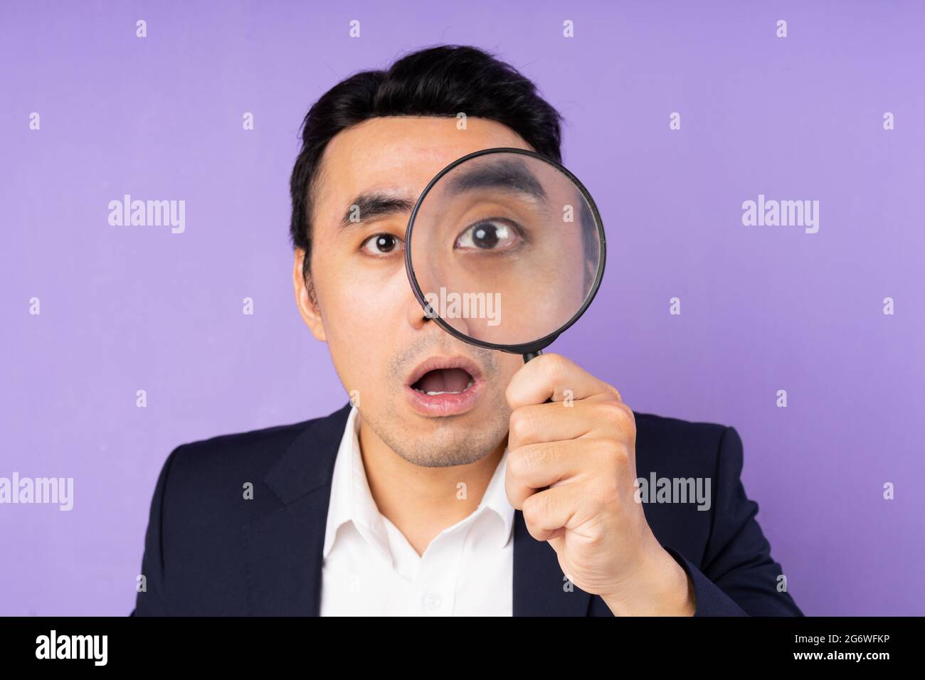 Business man in suit wearing magnifying glass, isolated on purple background Stock Photo