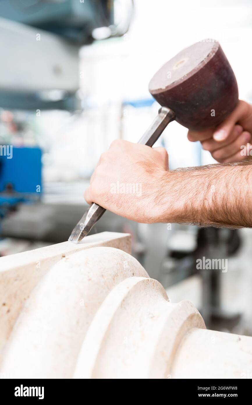 Stone carver working with hammer and chisel at marble column Stock