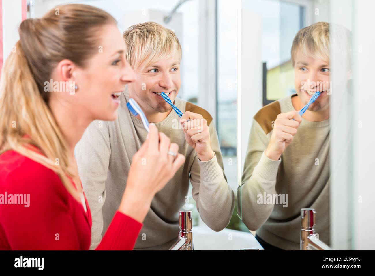Happy blond man holding a toothbrush while looking in the mirror next to his beautiful wife in the showroom of a modern sanitary ware shop Stock Photo