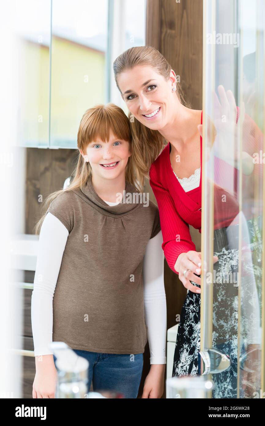 Cheerful woman with her daughter looking at a shower cabin in the showroom of a sanitary ware shop with modern bathroom fixtures for sale Stock Photo