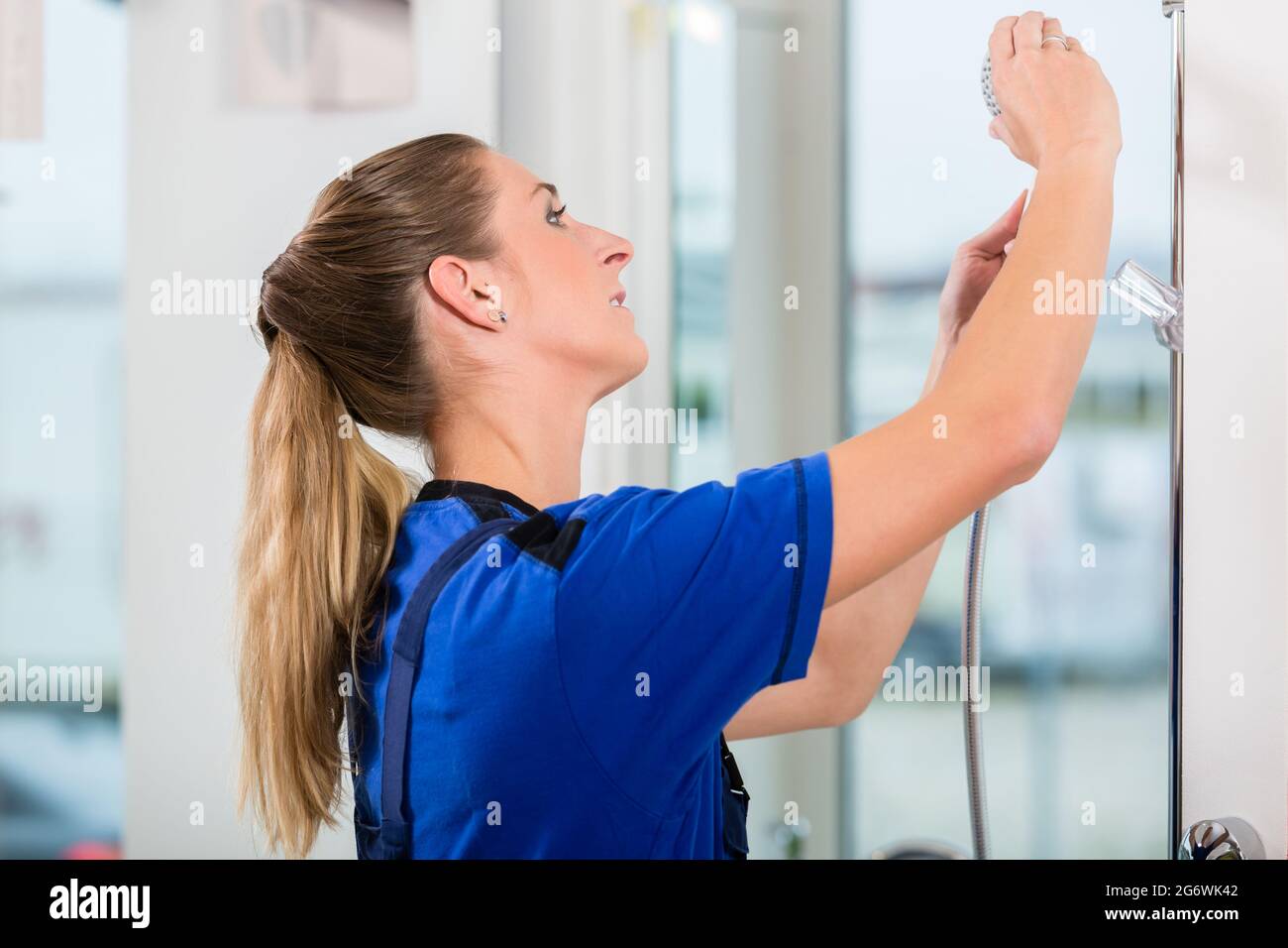Side view of a skilled female worker checking a showerhead during quality control in the showroom of a modern sanitary ware shop Stock Photo