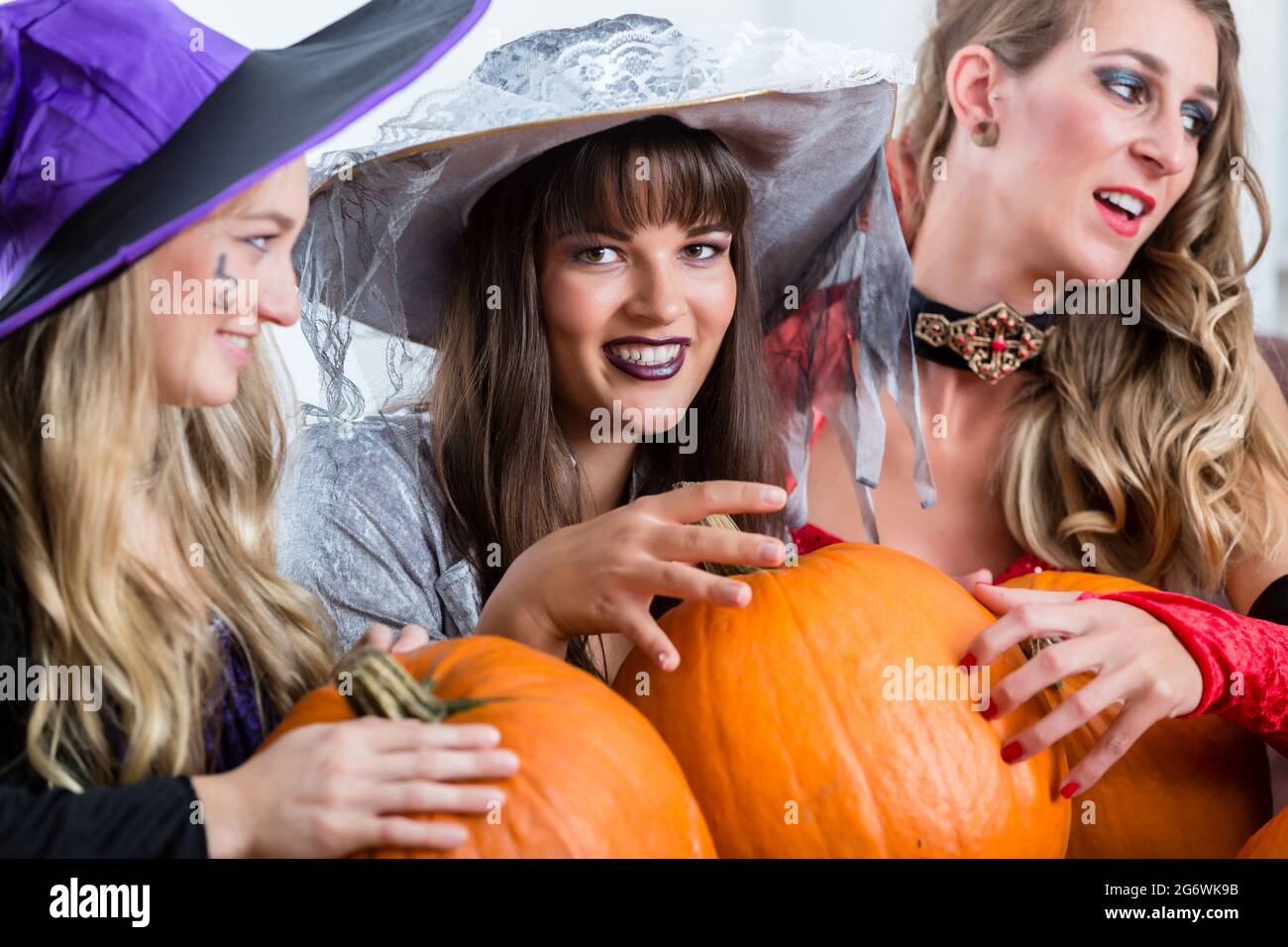 Three young and beautiful women wearing funny party costumes while acting as witches joining their malicious forces at Halloween Stock Photo