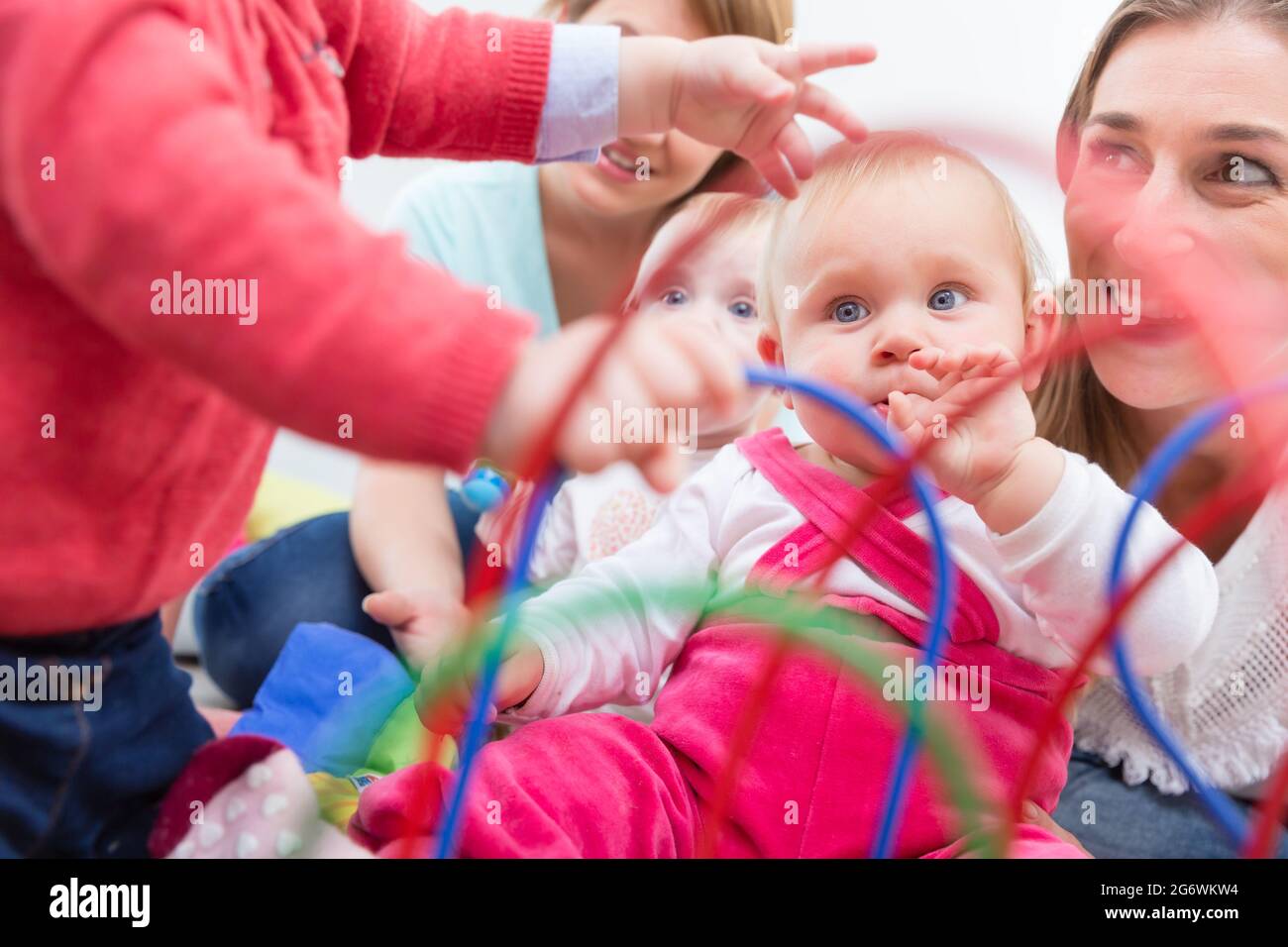Group of happy young mothers watching their cute and healthy babies while playing with multicolored toys in a modern daycare center Stock Photo