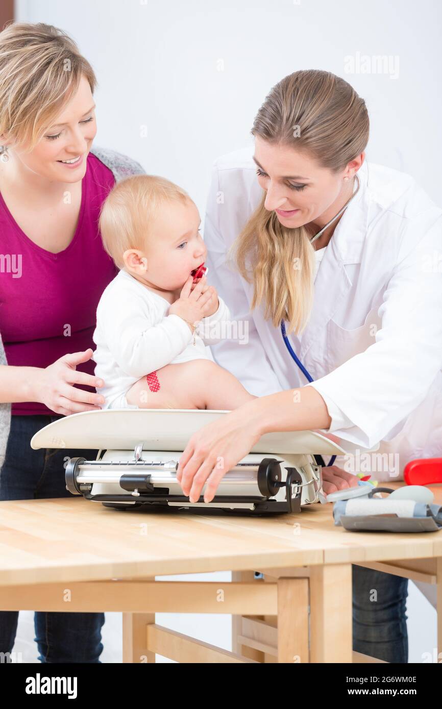Female pediatric care specialist smiling, while measuring the weight of