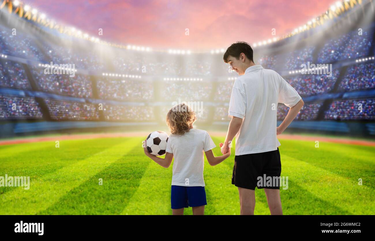 Football game on stadium. Young player and little boy play soccer on outdoor field. Supporter and coach watching match. Brothers exercise. Stock Photo