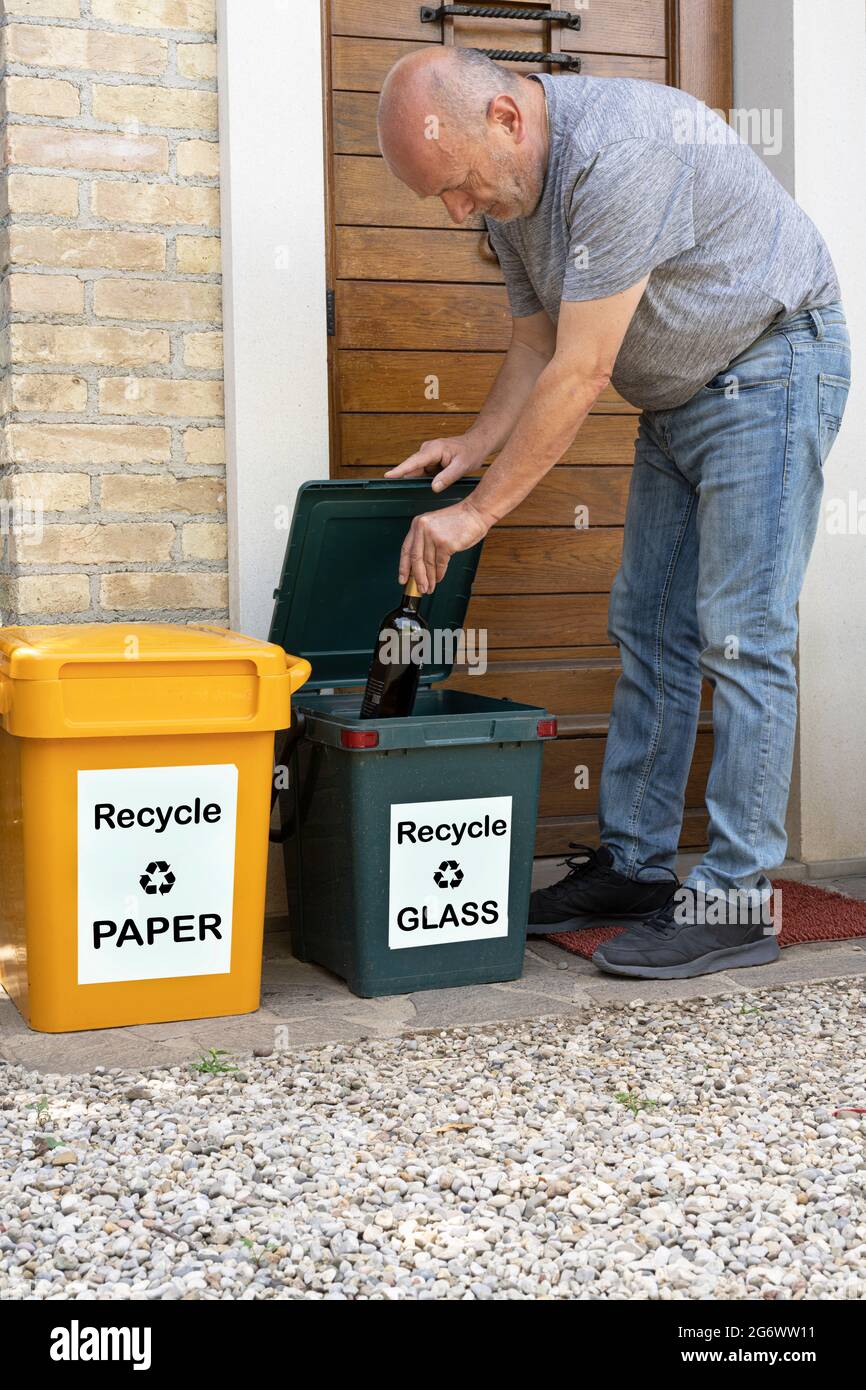 a man puts a bottle in the glass recycling bin in front of his house Stock Photo