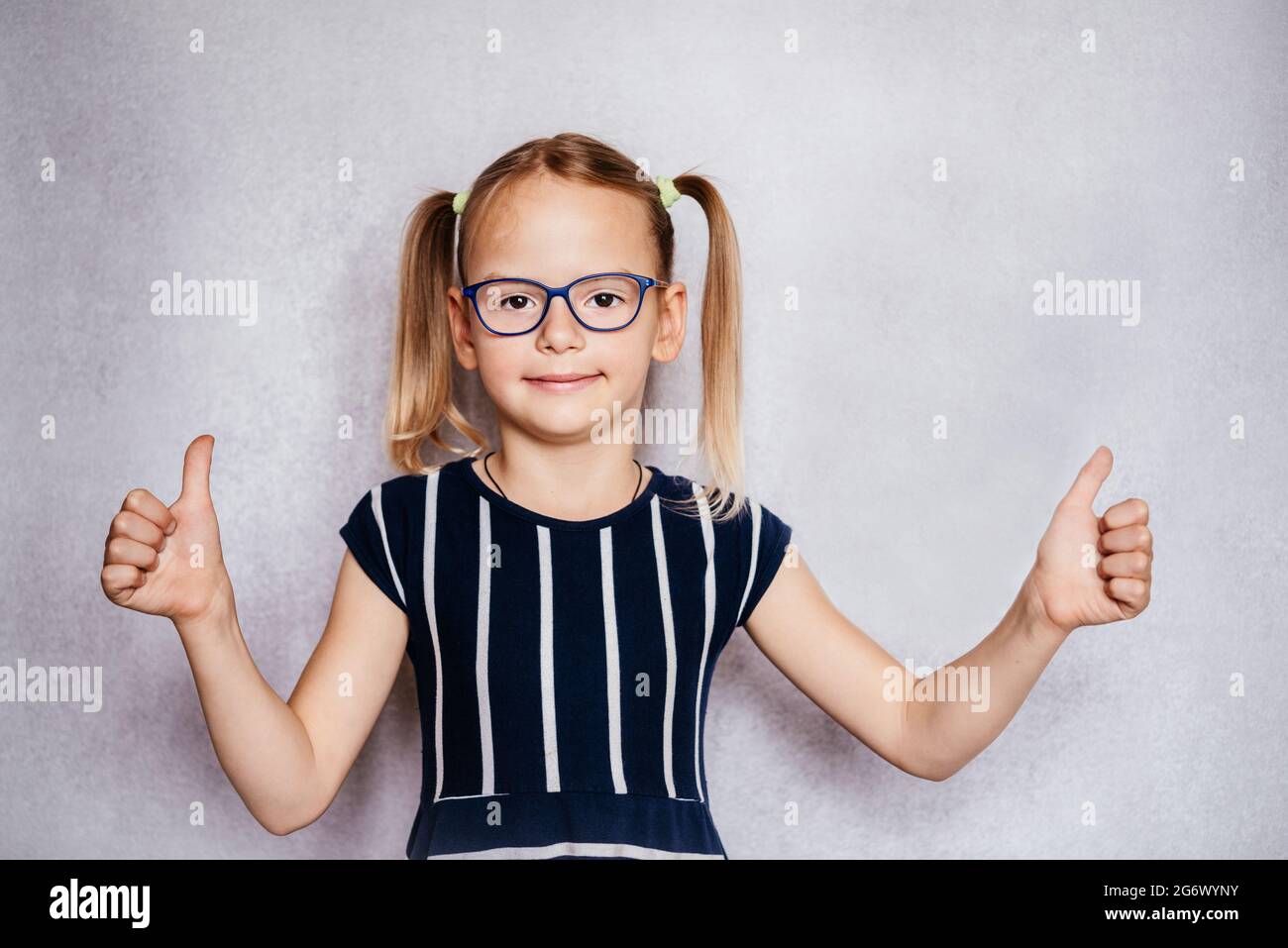Little girl wearing eyeglasses with her thumbs up, children's Pediatric Ophthalmology, common eye problems in children Stock Photo