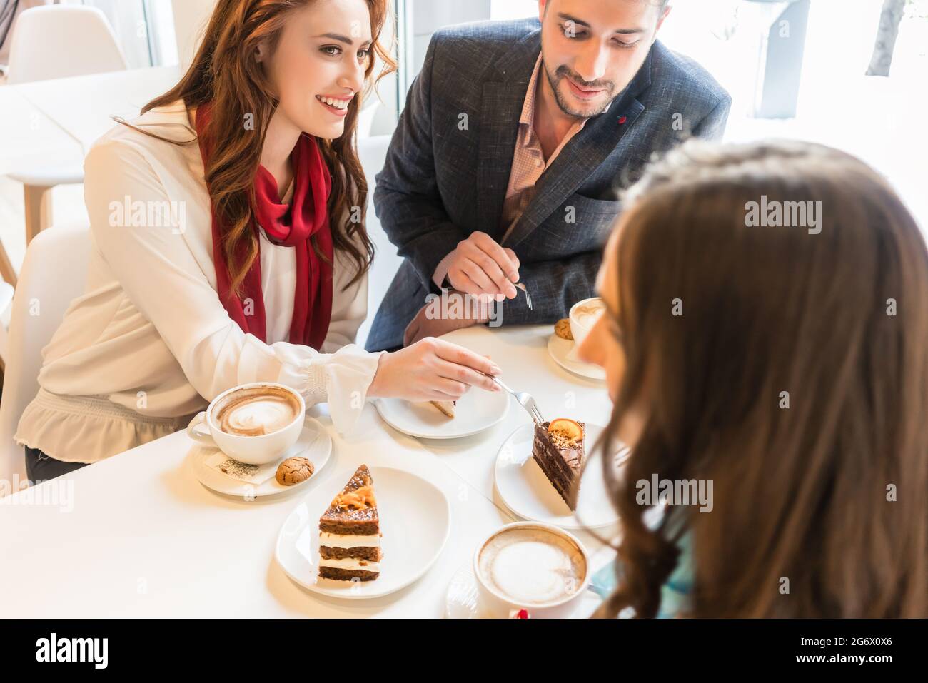 High-angle view of a happy couple sharing cakes while sitting at table with their mutual friend in a trendy coffee shop Stock Photo
