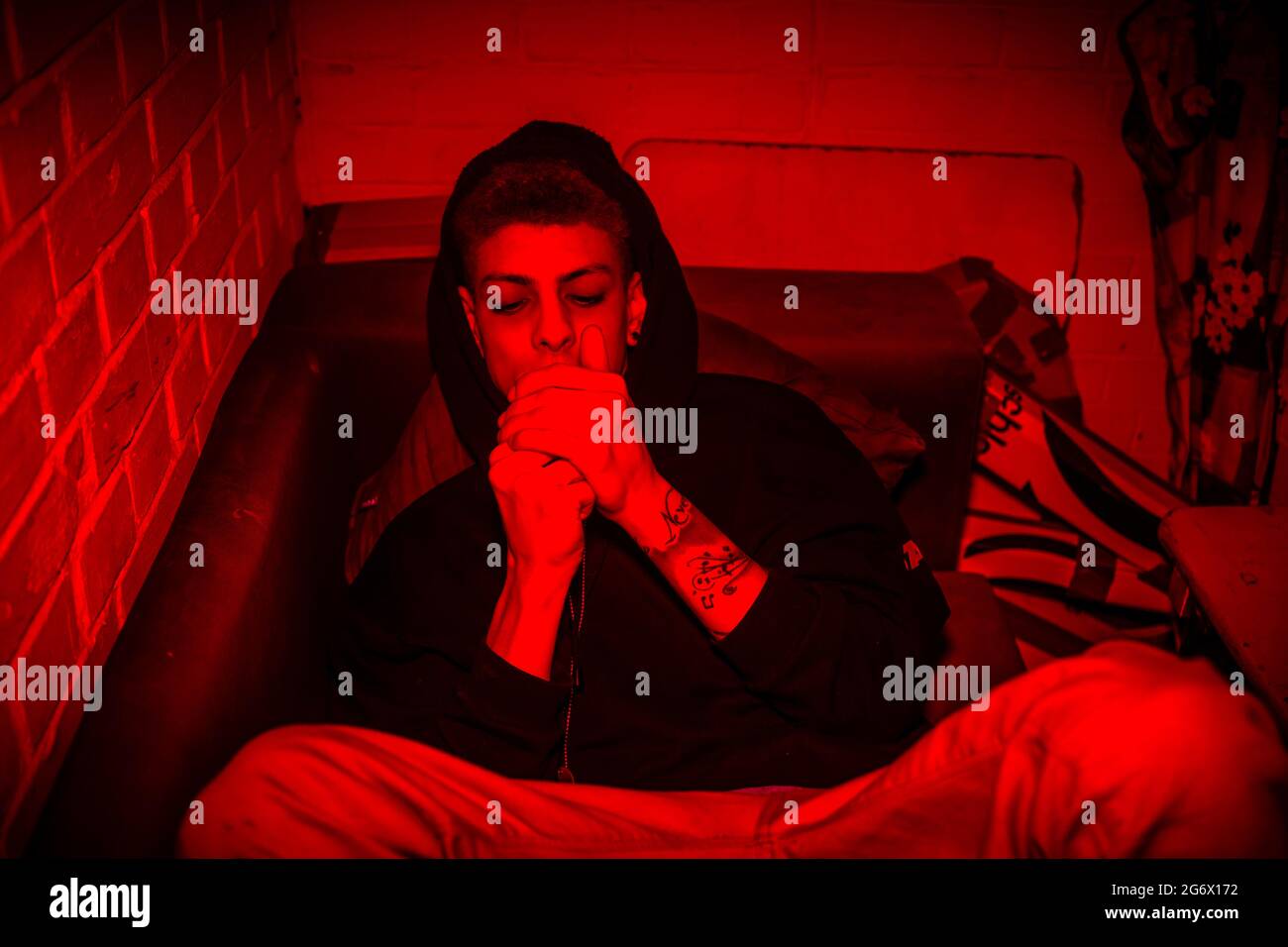 High-angle view of an addicted young man taking dangerous drugs orally while lying down on a couch in an obscure red light at home Stock Photo