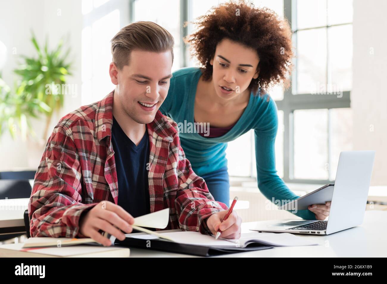 Two young students browsing internet for online useful up-to-date information while writing together an assignment in the interior of a modern univers Stock Photo